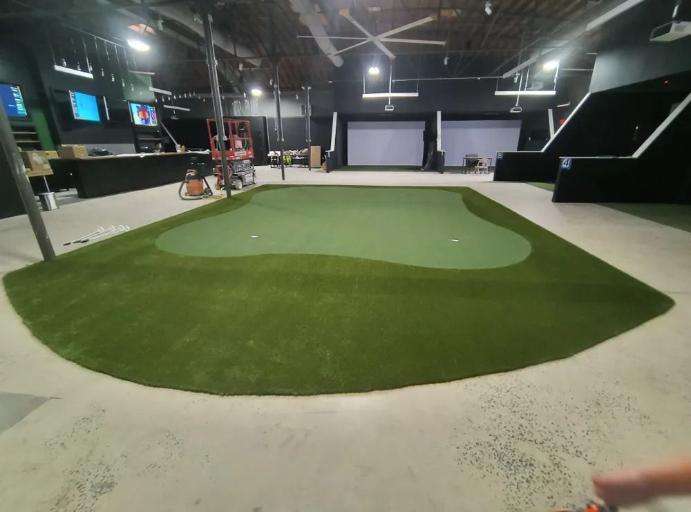 Indoor golf practice facility with green putting turf, sand trap, and simulator screens