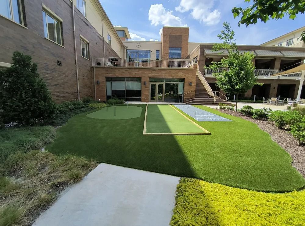 Courtyard with artificial turf, concrete path, and apartment-style buildings under a partly cloudy sky