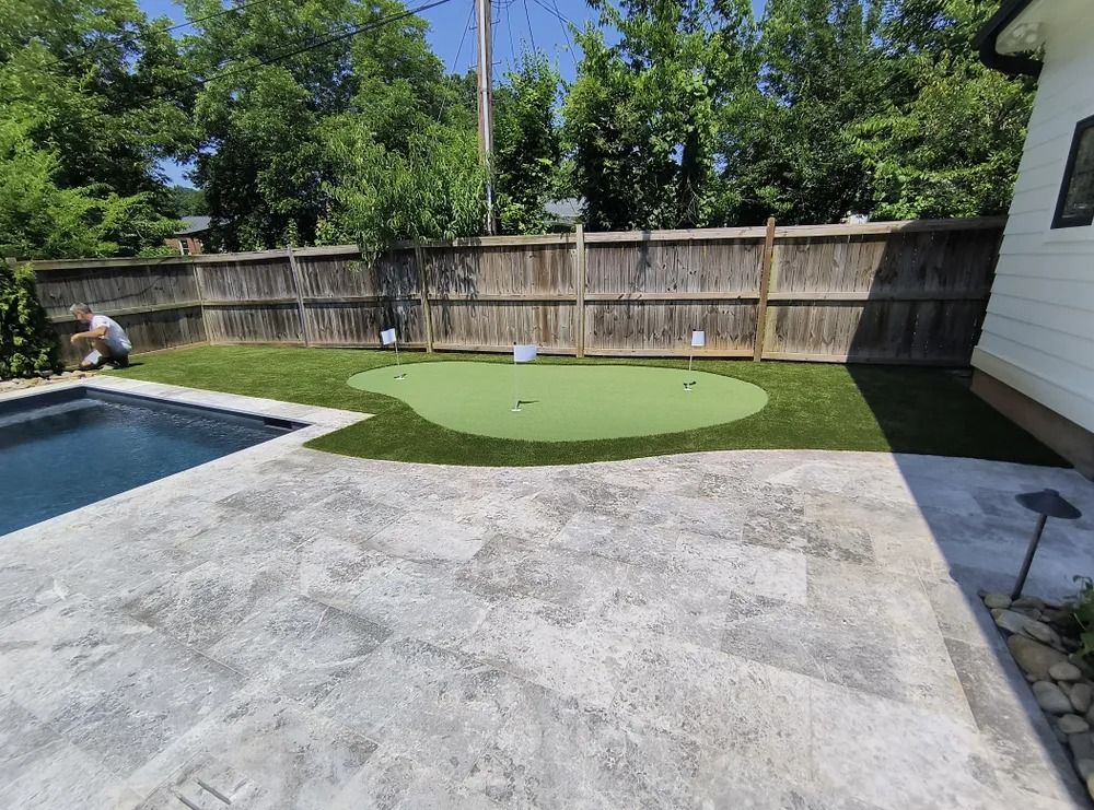 Backyard with swimming pool, concrete patio, putting green, and wooden fence under a clear sky
