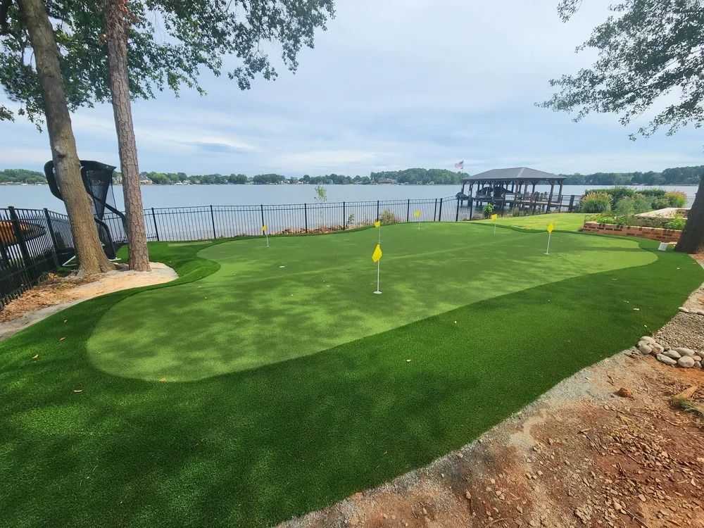 Small lakeside putting green with a flag, trees, and calm water in the background