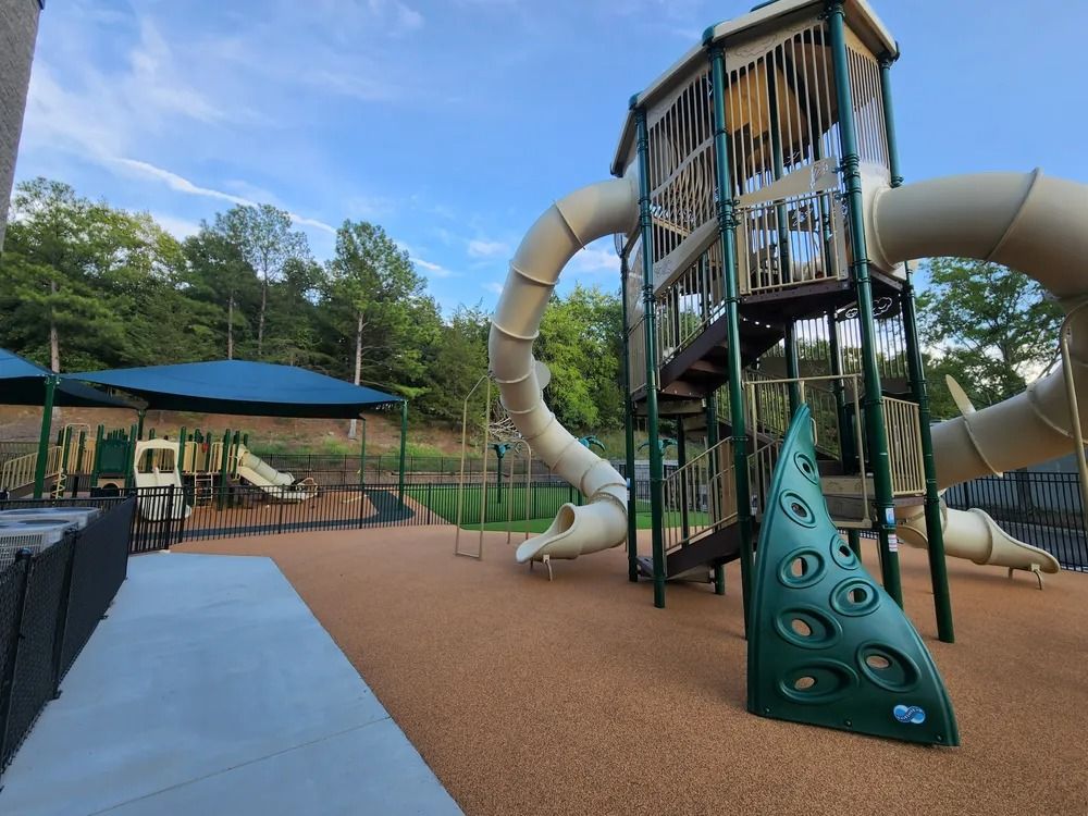 Outdoor playground with tall slide tower, twisting tube slides, and blue shade sails by a fenced area