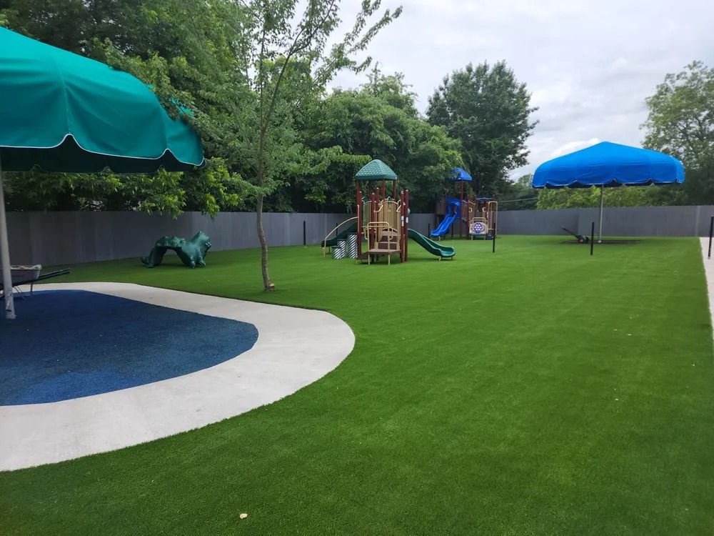 Playground with a blue splash pad, green lawn, shade umbrellas, and play structures under a cloudy sky