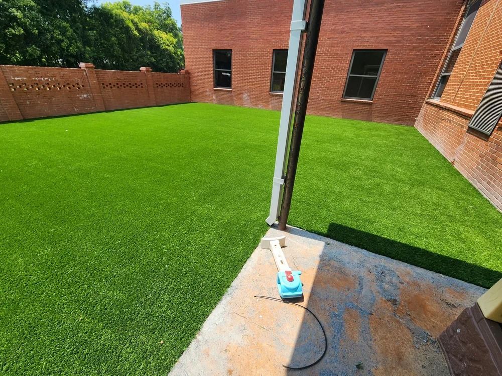 Small backyard patio with bright green turf, brick walls, and a pressure washer on the concrete slab