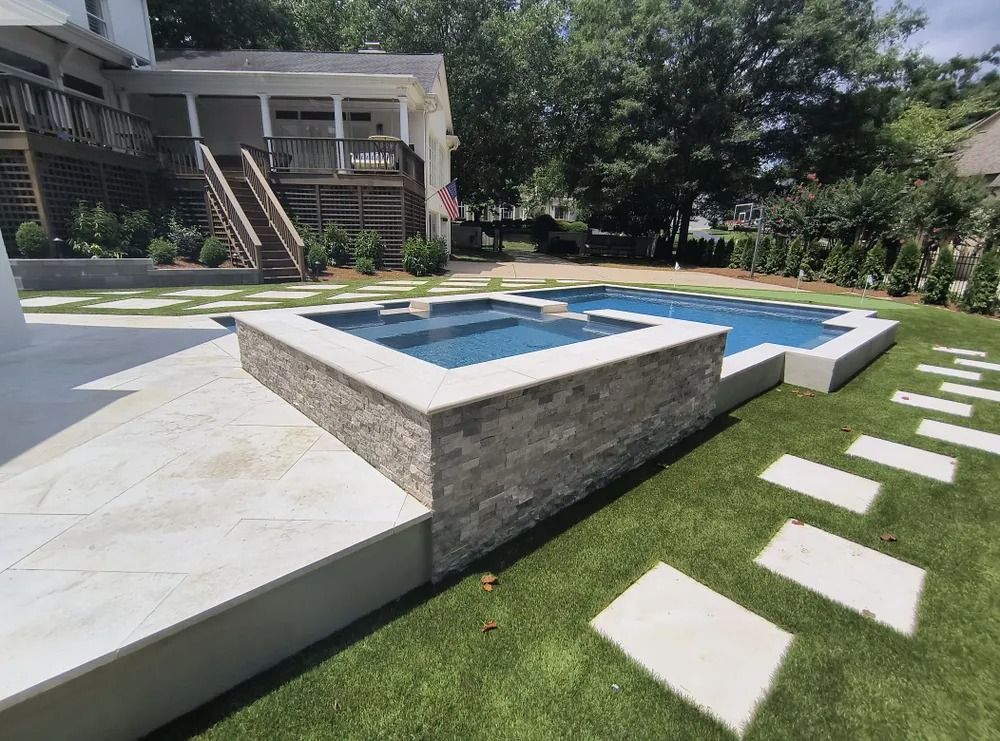 Backyard pool with stone hot tub, blue water, lawn stepping stones, and a house in the background