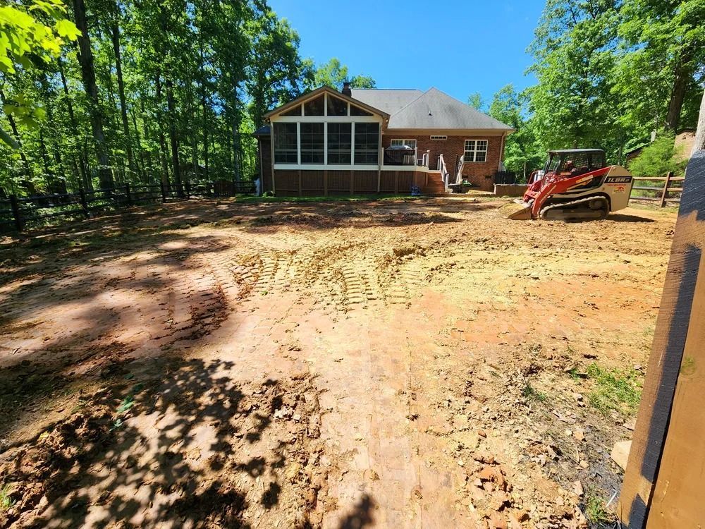 Cleared yard beside brick house with a red skid steer and fresh dirt grading