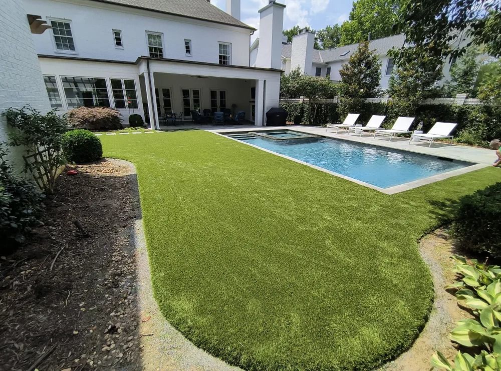 Backyard patio with a rectangular pool, white lounge chairs, and a green lawn beside a white house