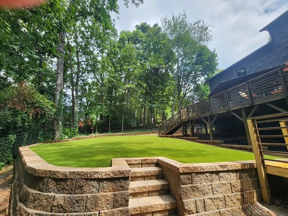 Stone terrace with steps leading to a manicured green lawn beside a wooden deck and trees
