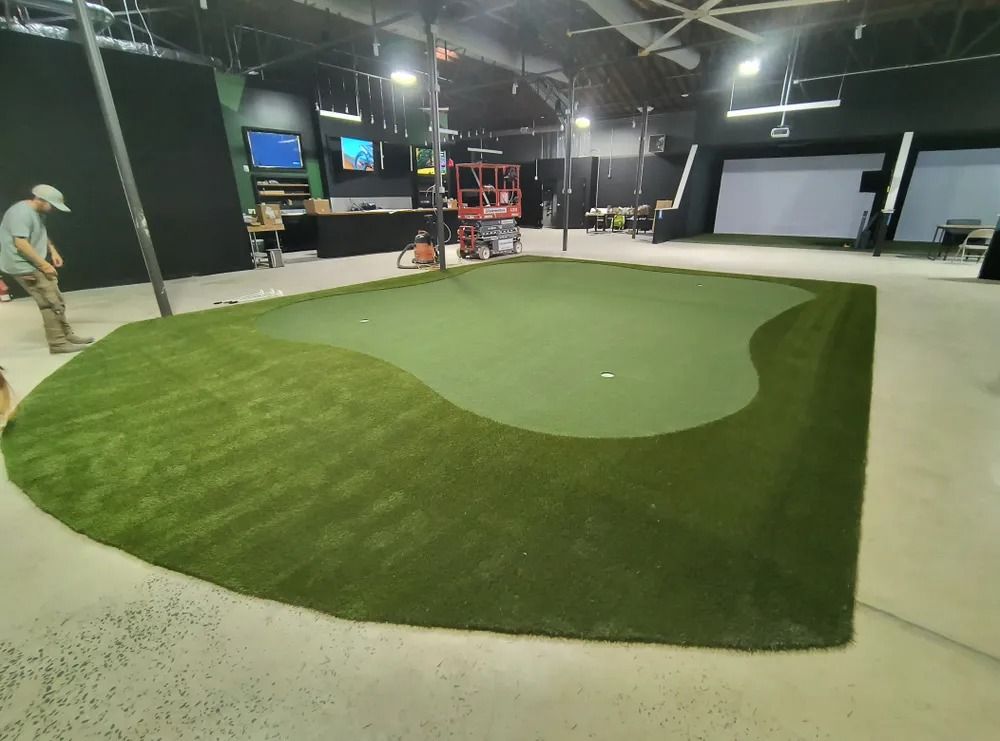 Indoor golf putting green with a curved two-tone turf surface and a worker in the background