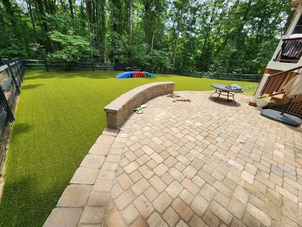 Backyard patio with curved stone bench, brick pavers, green lawn, trees, and a picnic table