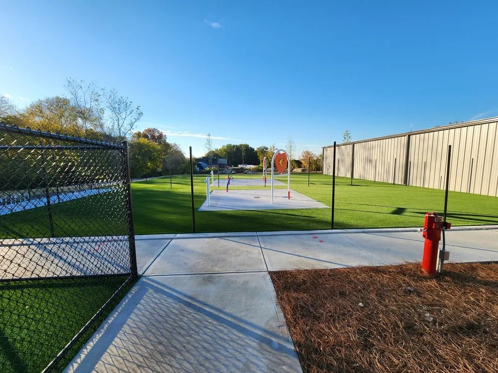 Outdoor exercise path with green lawn, concrete pad, chain-link fence, and red fire hydrant under blue sky