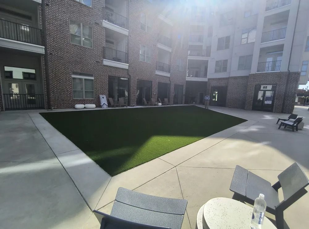 Apartment courtyard with a central green lawn, brick buildings, and patio chairs in bright sunlight