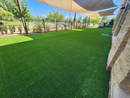 Shaded artificial grass courtyard with trees and stone walls beside a building