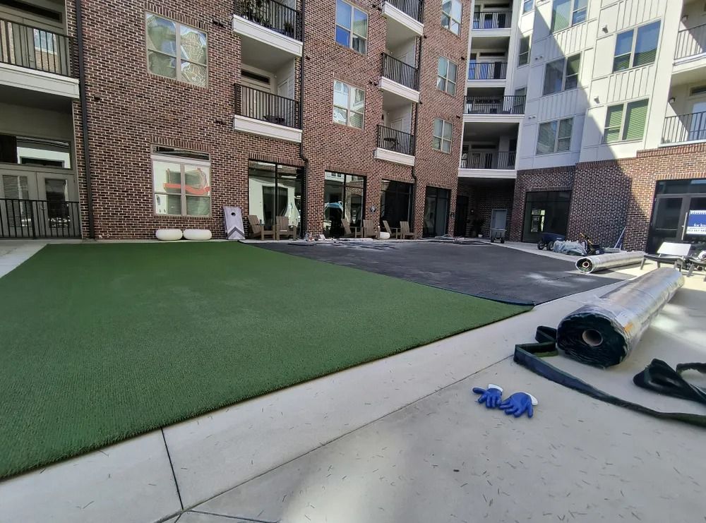 Apartment courtyard with artificial turf, concrete path, and a black tarp rolled on the right side