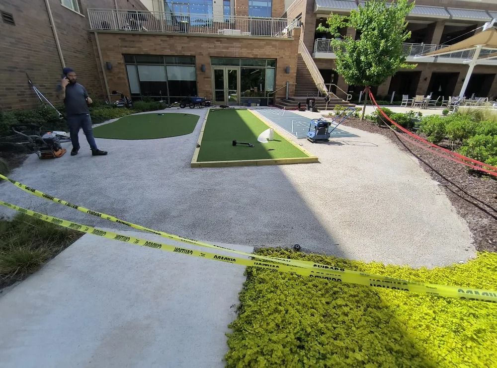 Outdoor courtyard with caution tape, workers, and newly laid turf and gravel near an apartment building