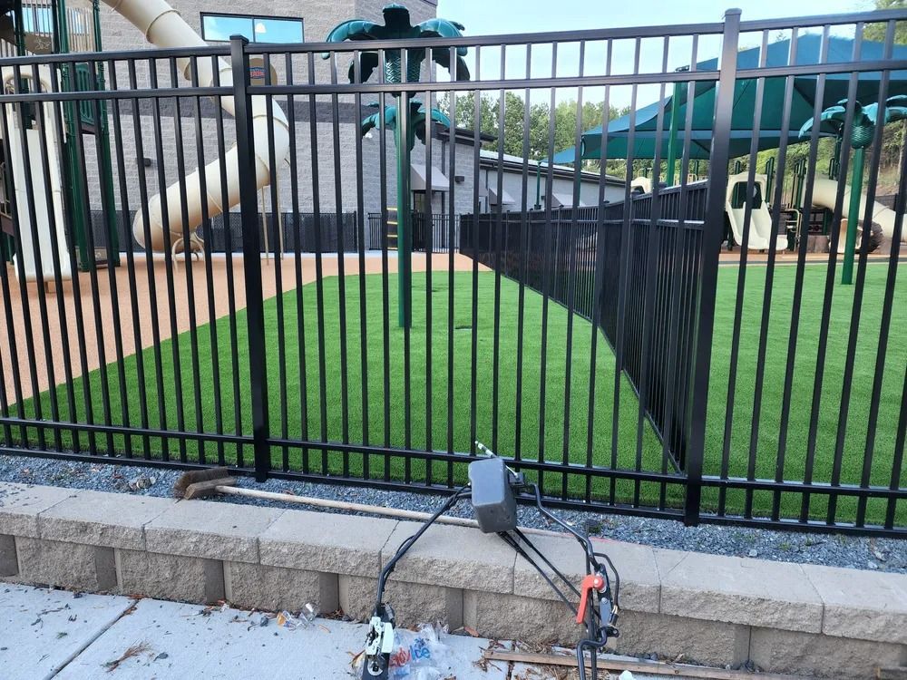Black metal fence around a grassy area with equipment on the pavement in the foreground