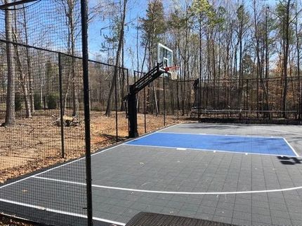 Outdoor basketball court with a hoop, black fencing, and surrounding trees in a wooded area