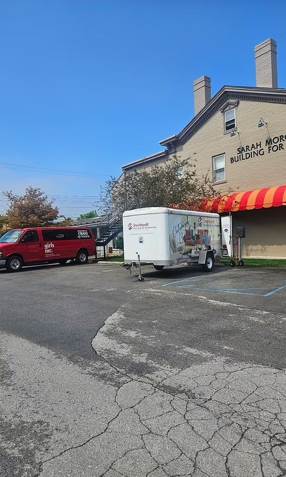 Red van and white trailer parked outside a stone building with a red-and-yellow awning.