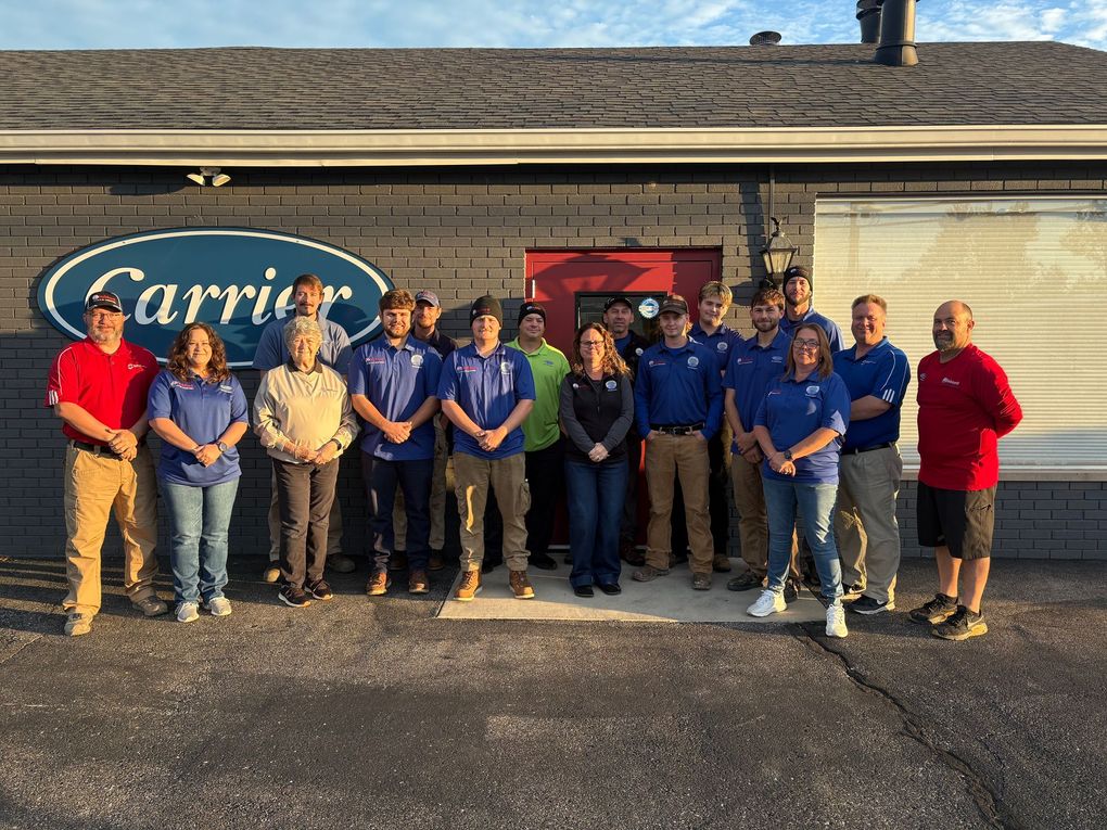 Group of employees posing outside a Carrier building, with the Carrier logo visible behind them.