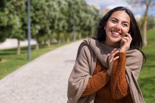 Smiling woman in a brown sweater sitting on a park path, resting her chin on her hand.