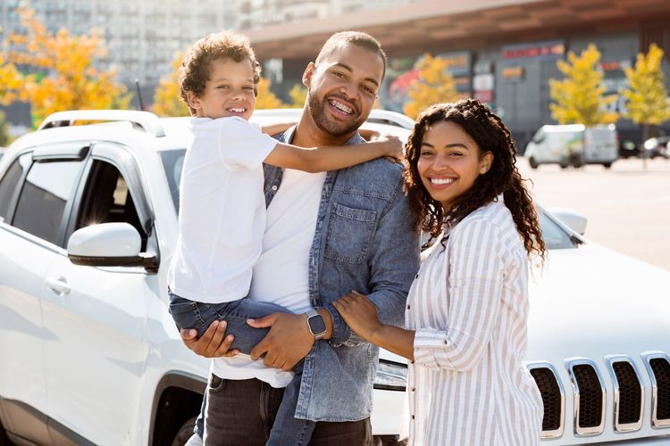 Family smiling beside a white SUV in a sunny parking lot
