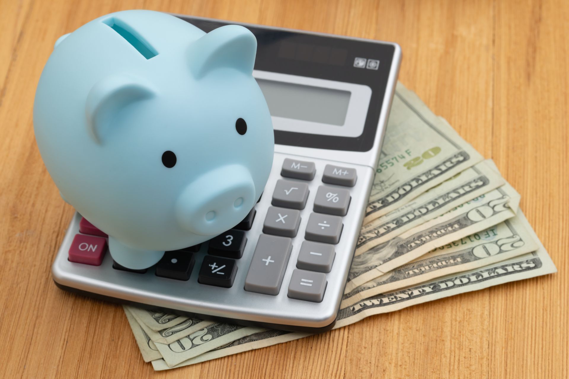 Blue piggy bank on a calculator with cash on a wooden table