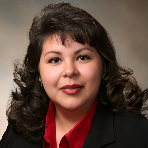 Woman in a navy blazer standing on a porch, smiling in front of a house.