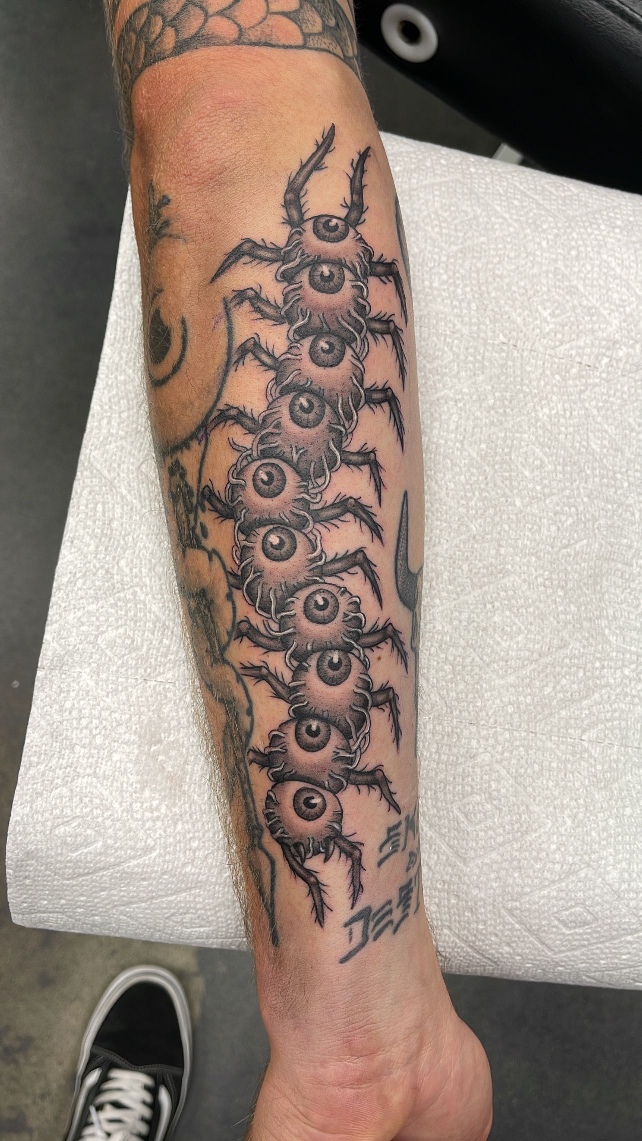 Forearm tattoo of a vertical row of detailed black eyes with swirling smoke-like patterns