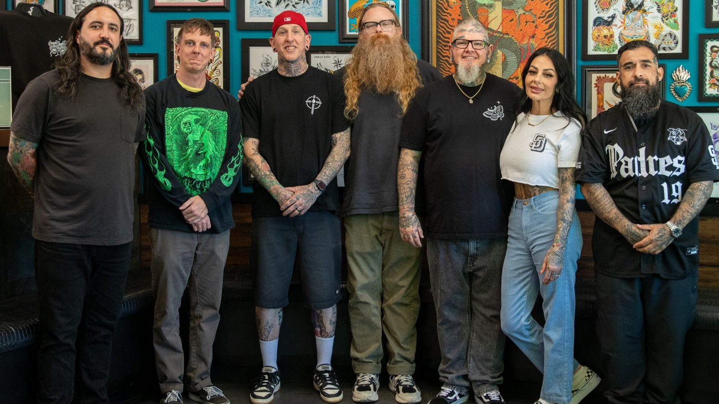 Seven people standing indoors in front of framed artwork, posing together and wearing casual dark clothes.