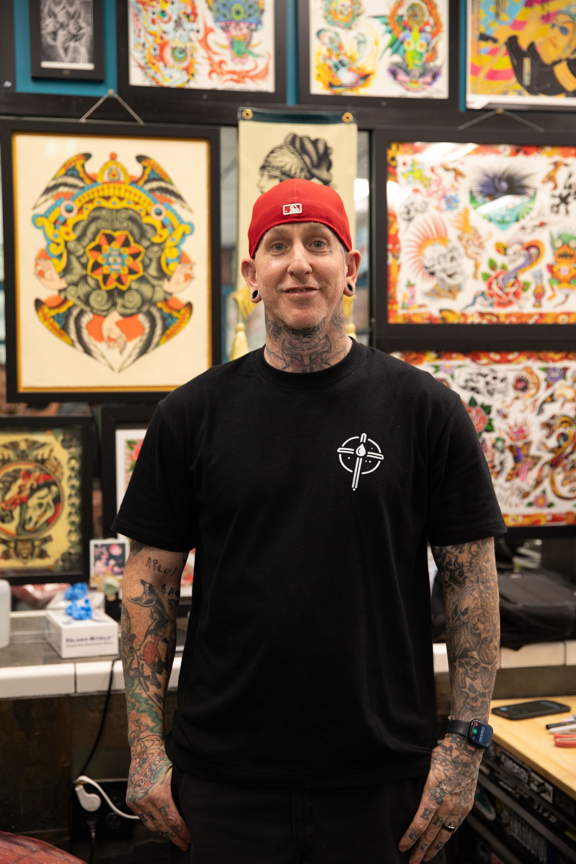 Person in a red cap and black shirt stands in front of colorful tattoo artwork display.