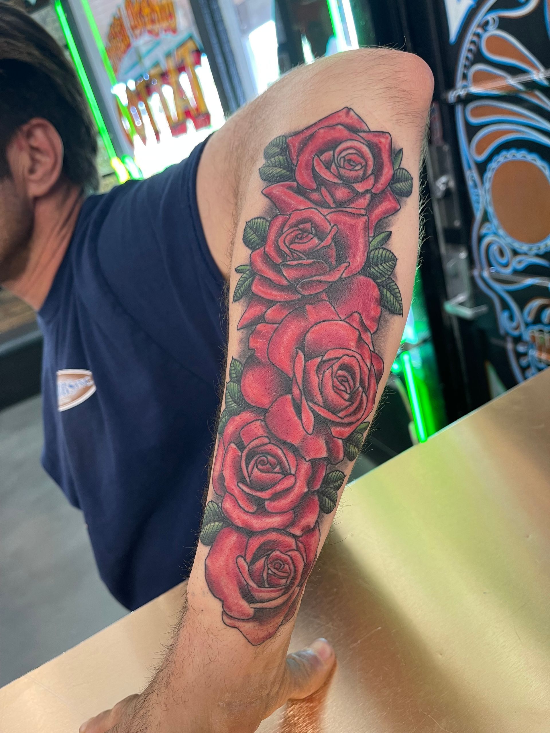 Forearm with a red rose tattoo, resting on a counter in a brightly lit interior.