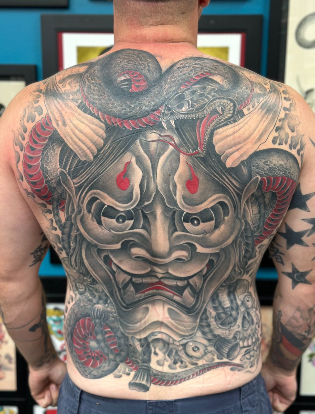Back tattoo of a fierce Japanese-style demon mask with snakes and red accents