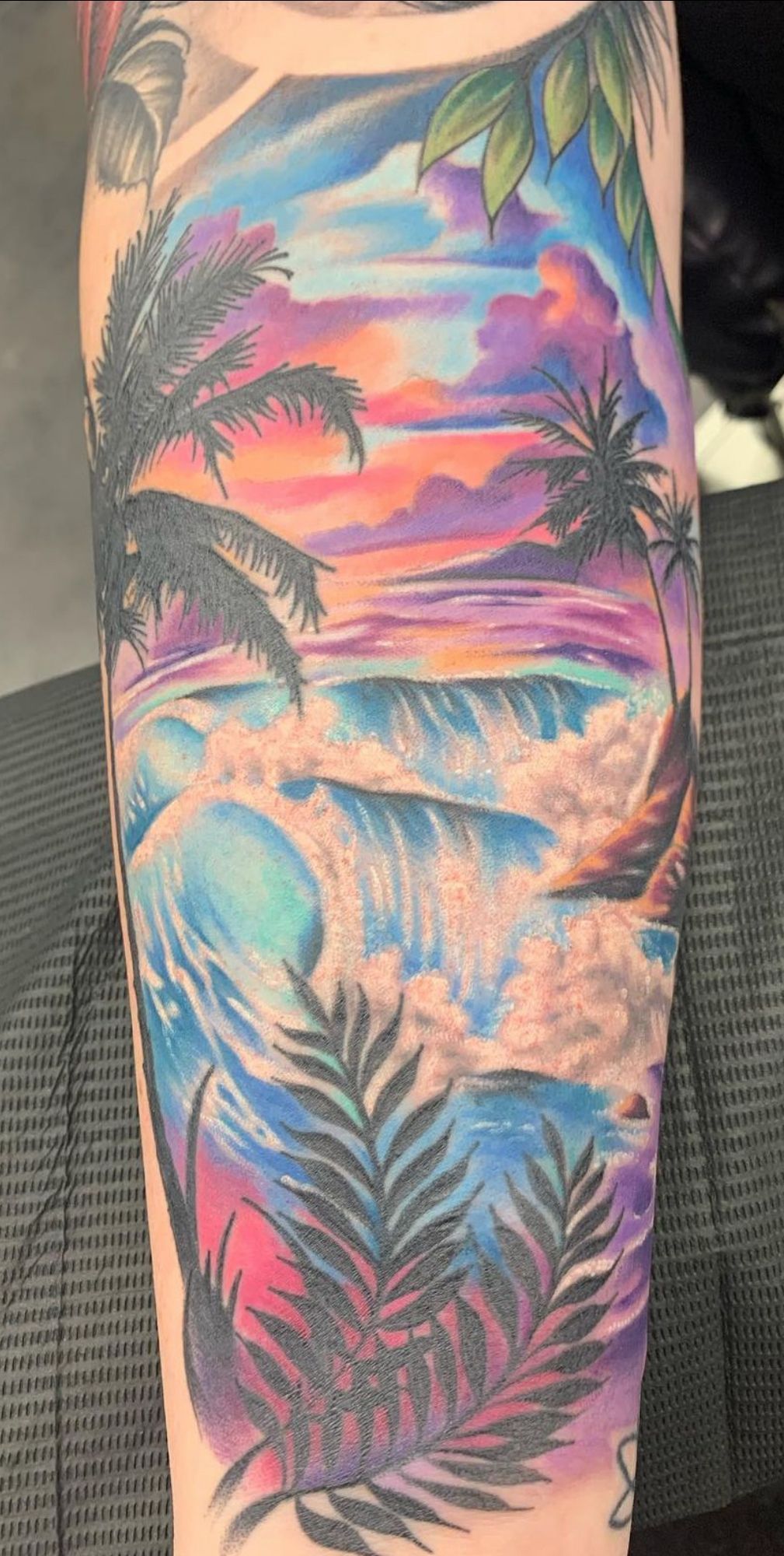 Colorful tropical sunset tattoo with palm trees and ocean waves on a leg