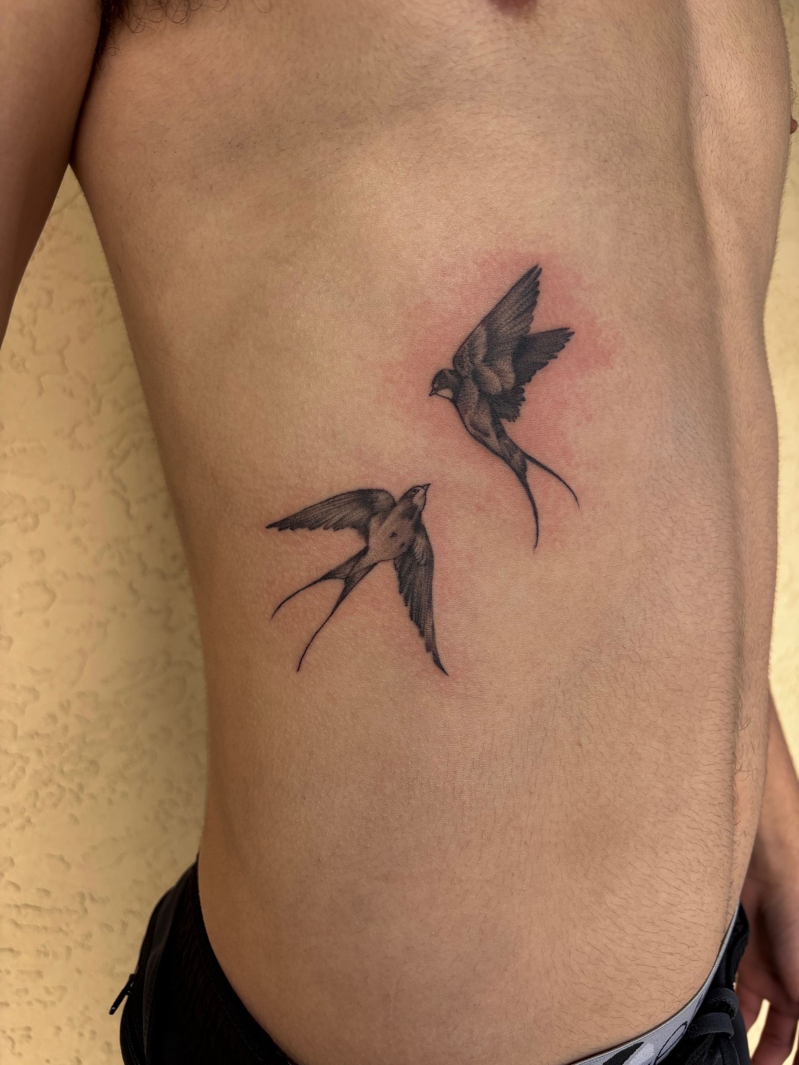 Two black hummingbird tattoos on a person's side, near the waist.