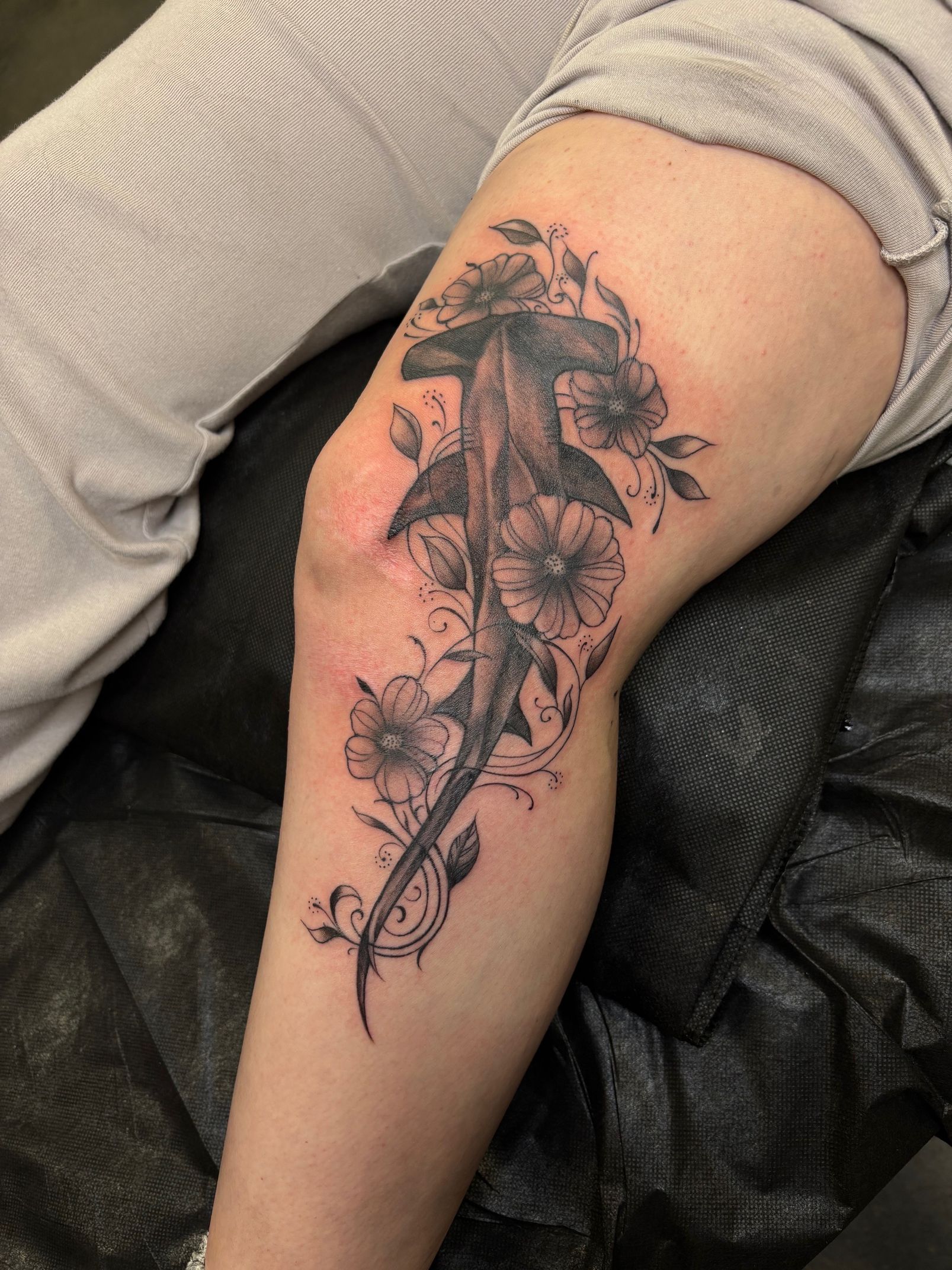Black floral tattoo on a person’s upper leg, shown close-up against gray fabric.