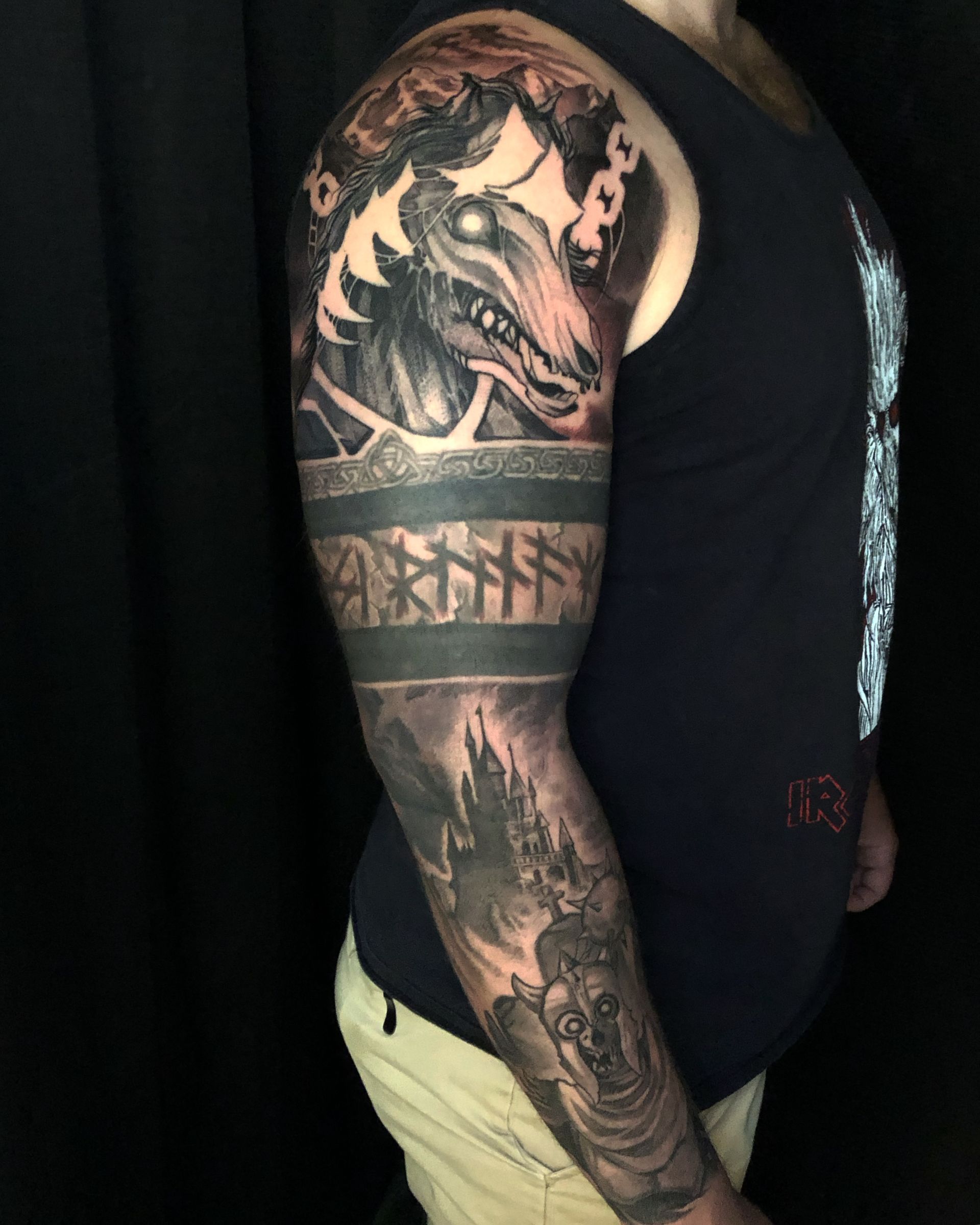 Side view of a tattooed person wearing a black tank top and yellow shorts against a dark background