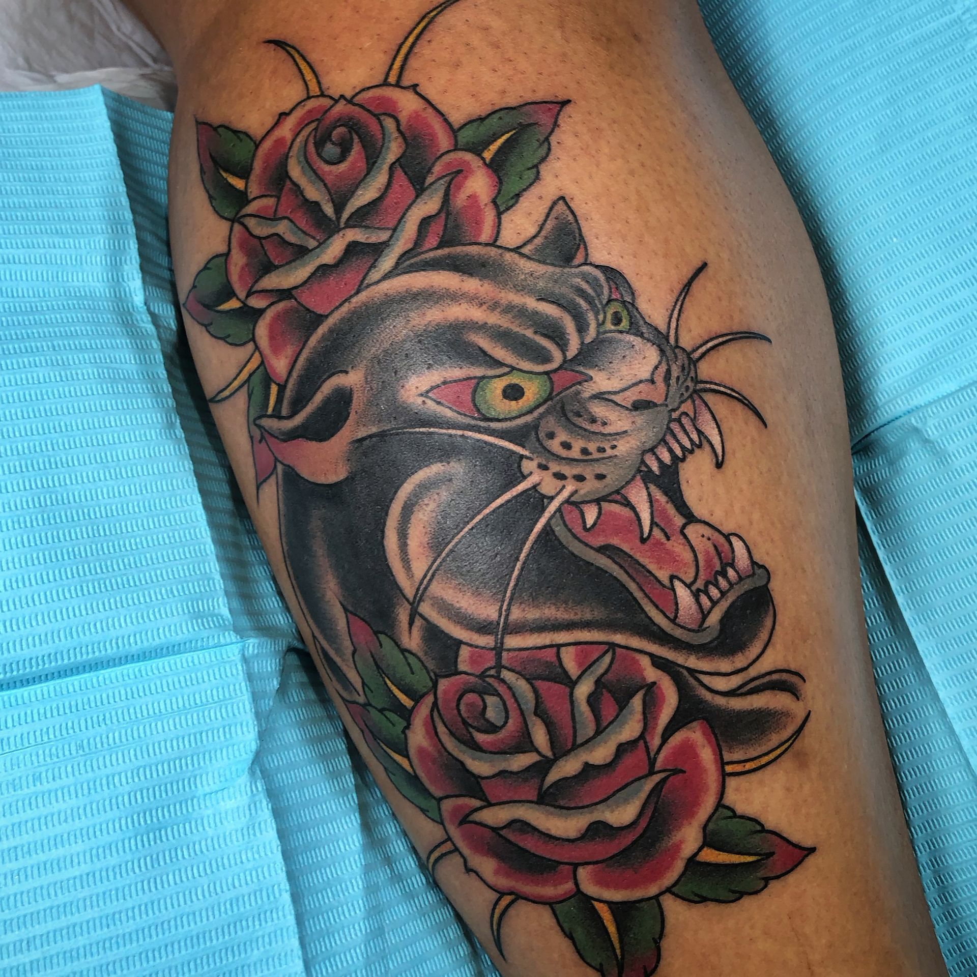 Black panther tattoo with red roses on a person’s calf