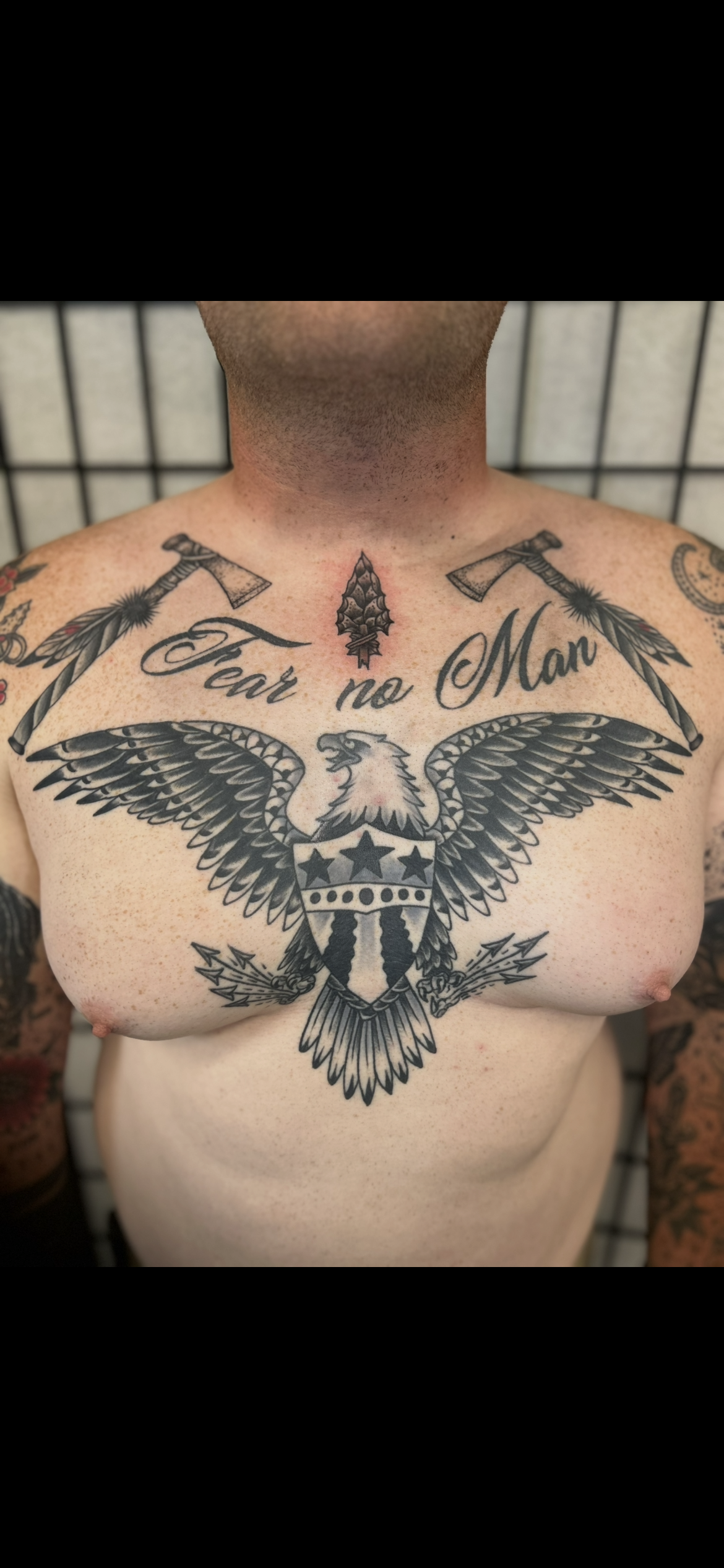 Torso with large eagle chest tattoo and script reading “For the Moment” across the upper chest