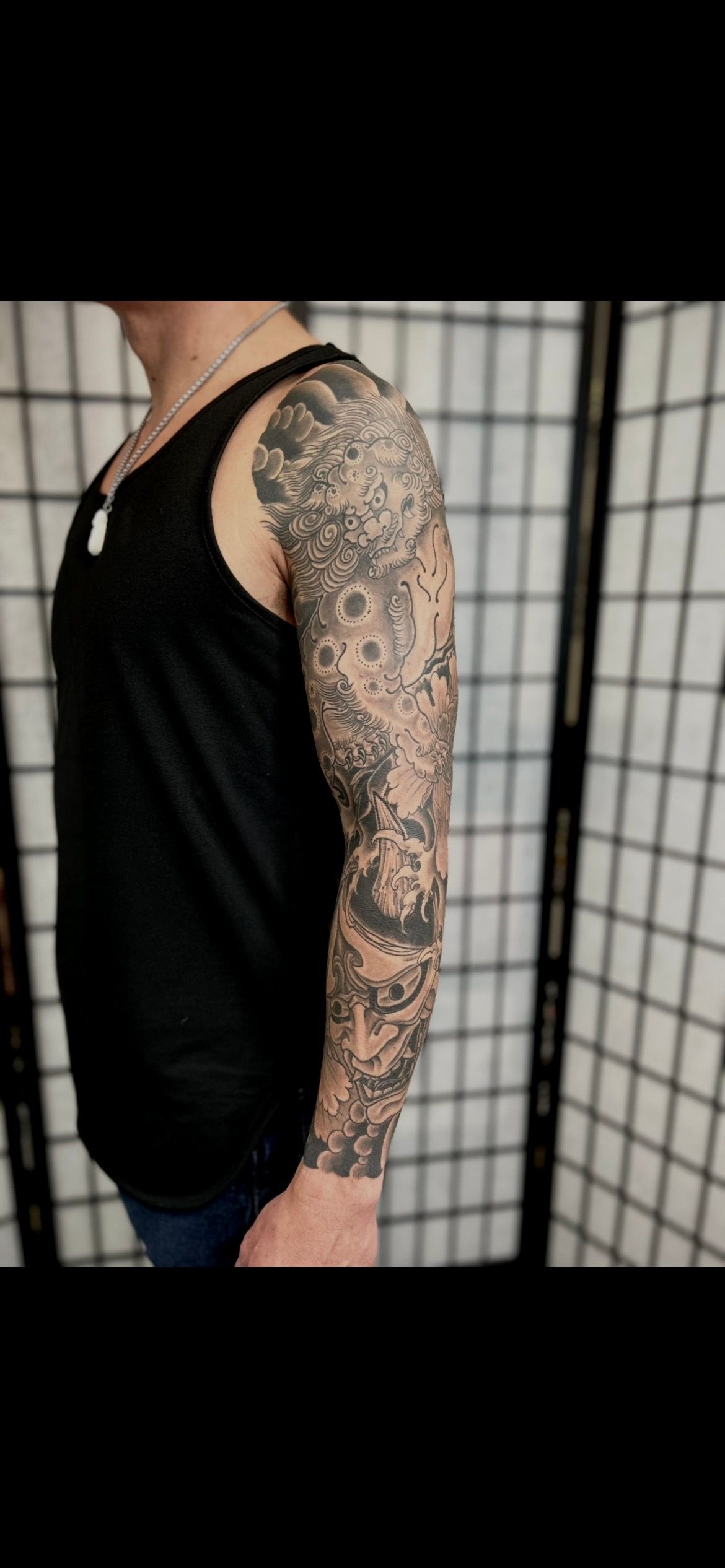 Side view of a person wearing a black tank top, showing a full tattoo sleeve on the arm.