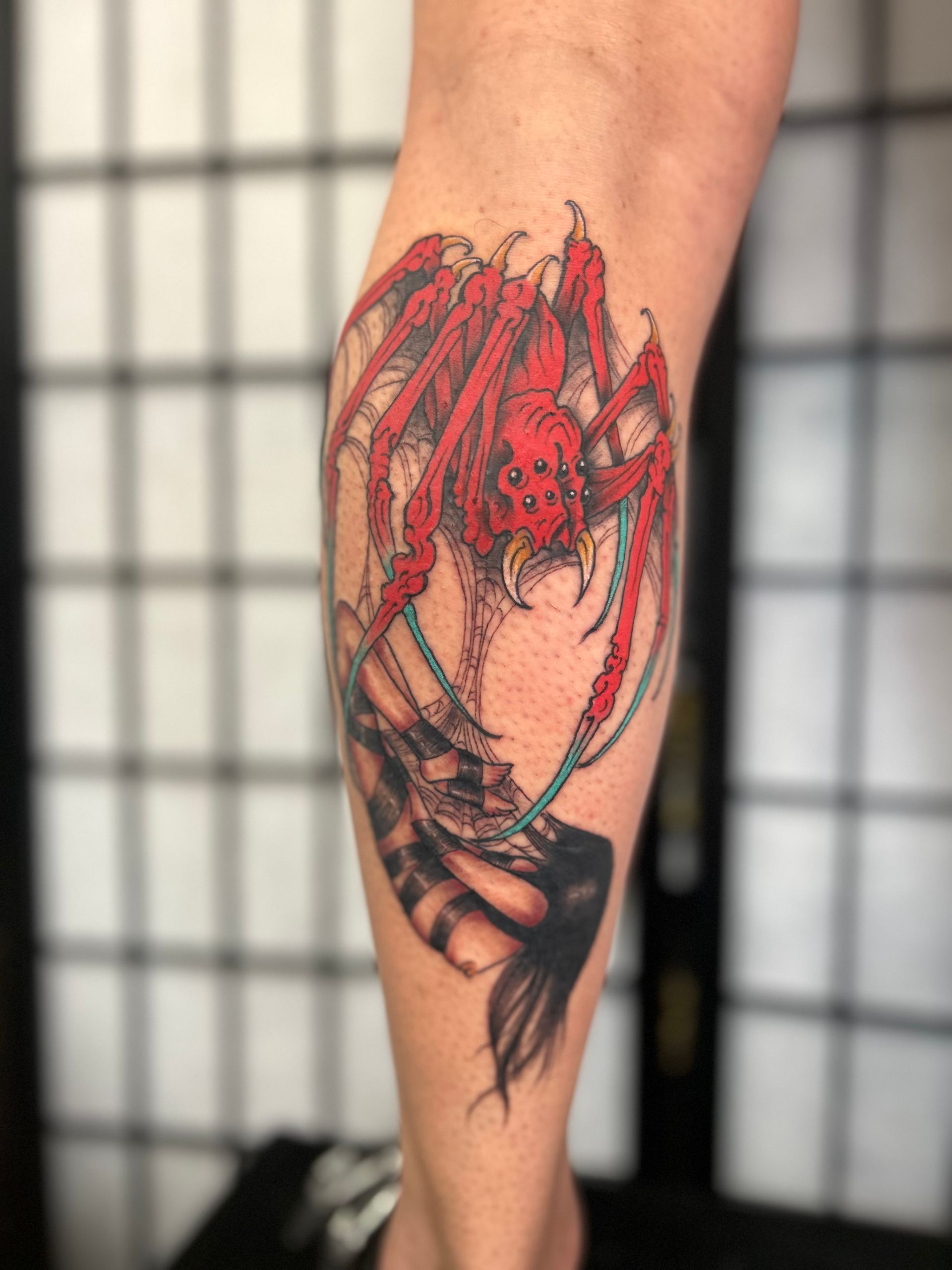 Red and black spider tattoo on an arm, with web-like details and a bold, sketchy style.