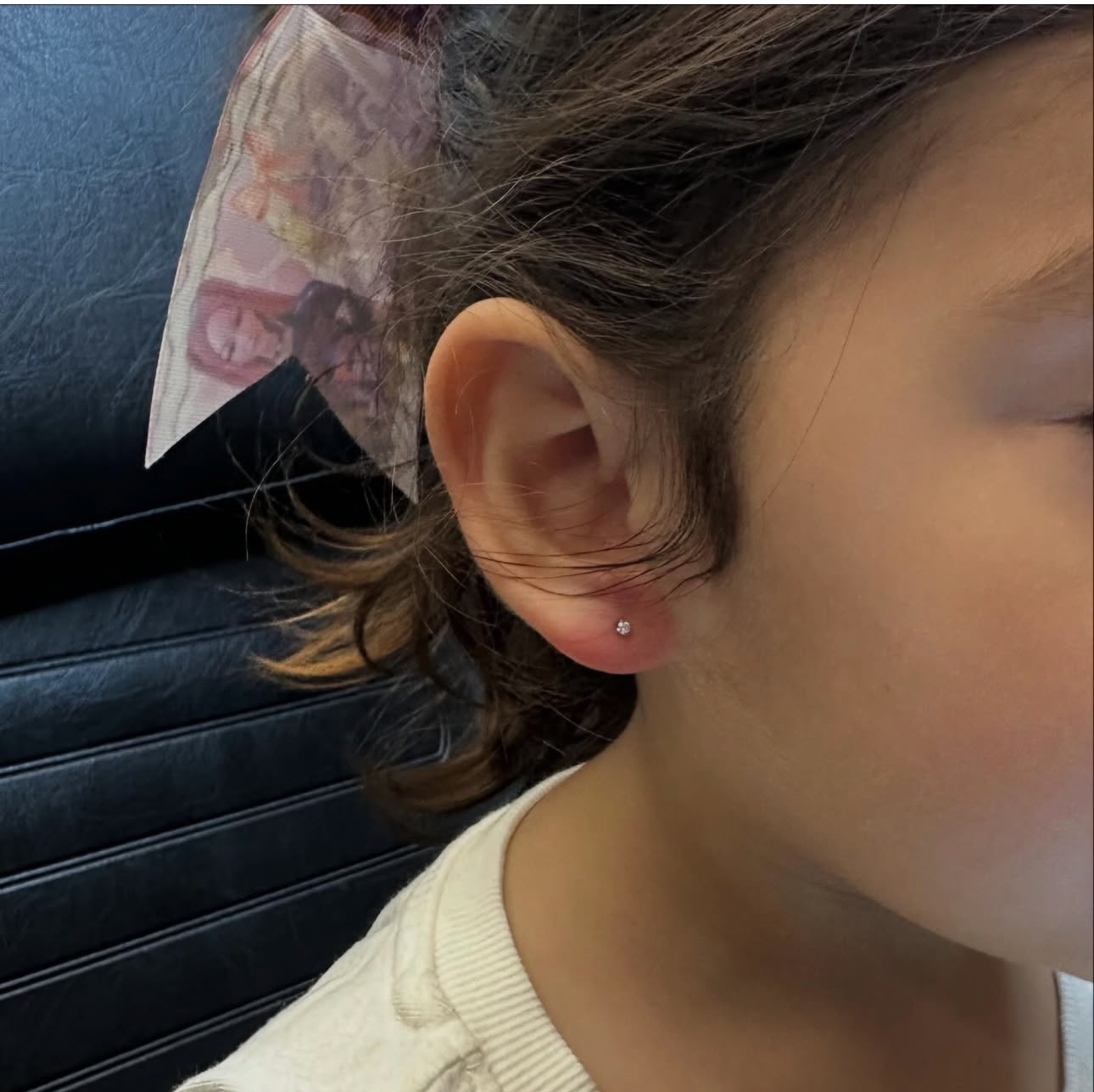 Close-up of a child's ear with a small stud earring and a pink patterned background