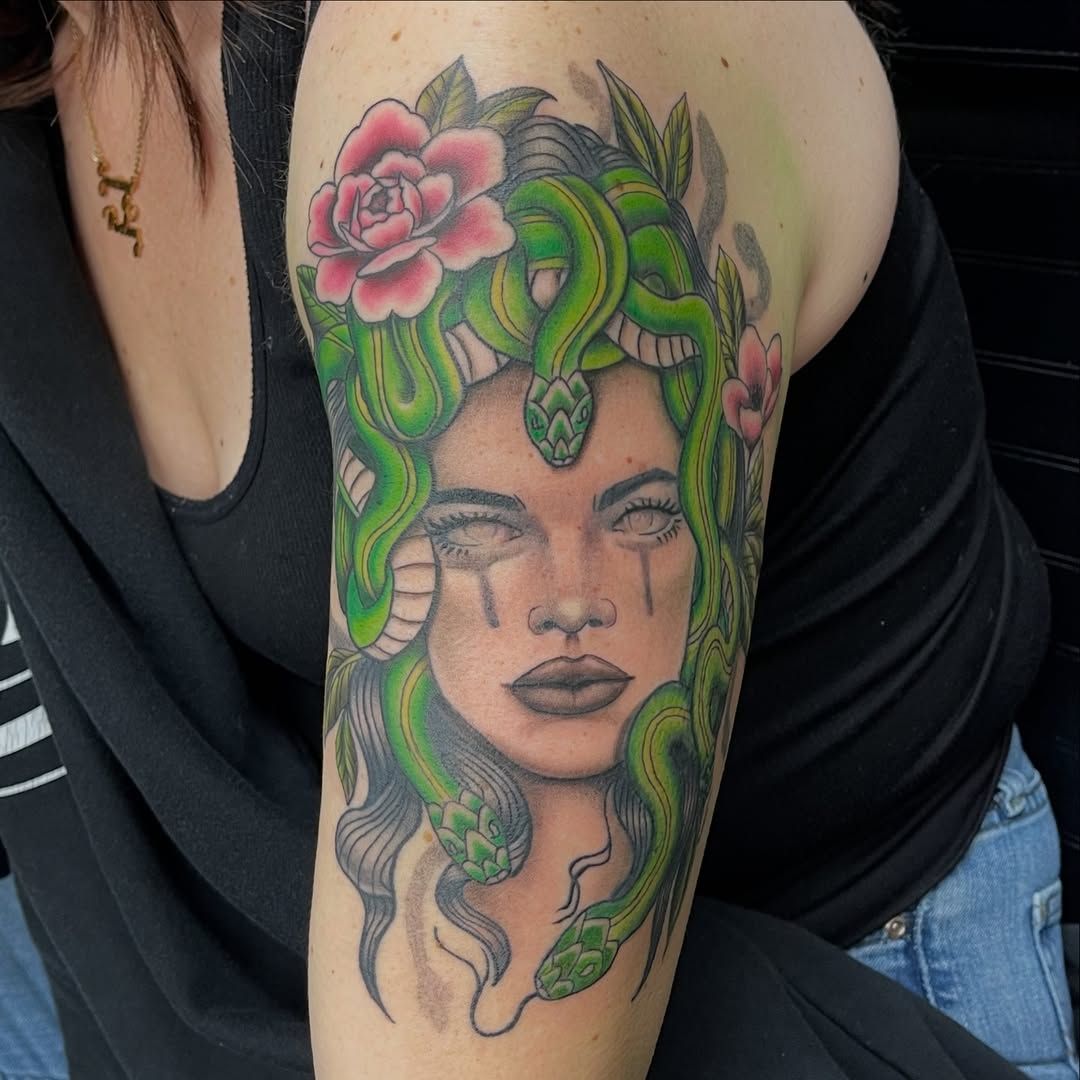 Colorful tattoo of a face with green hair and a pink flower on an upper arm