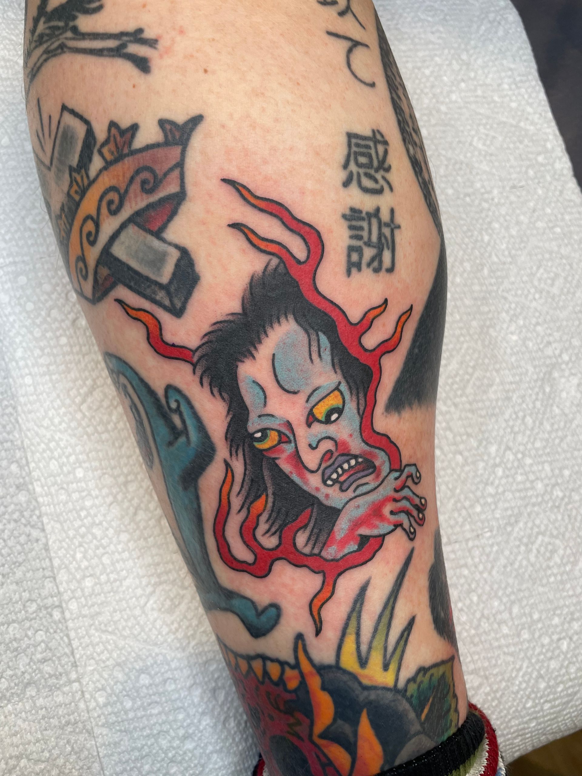 Colorful tattoo of a snarling red-and-black demon face with Japanese characters on a person’s arm
