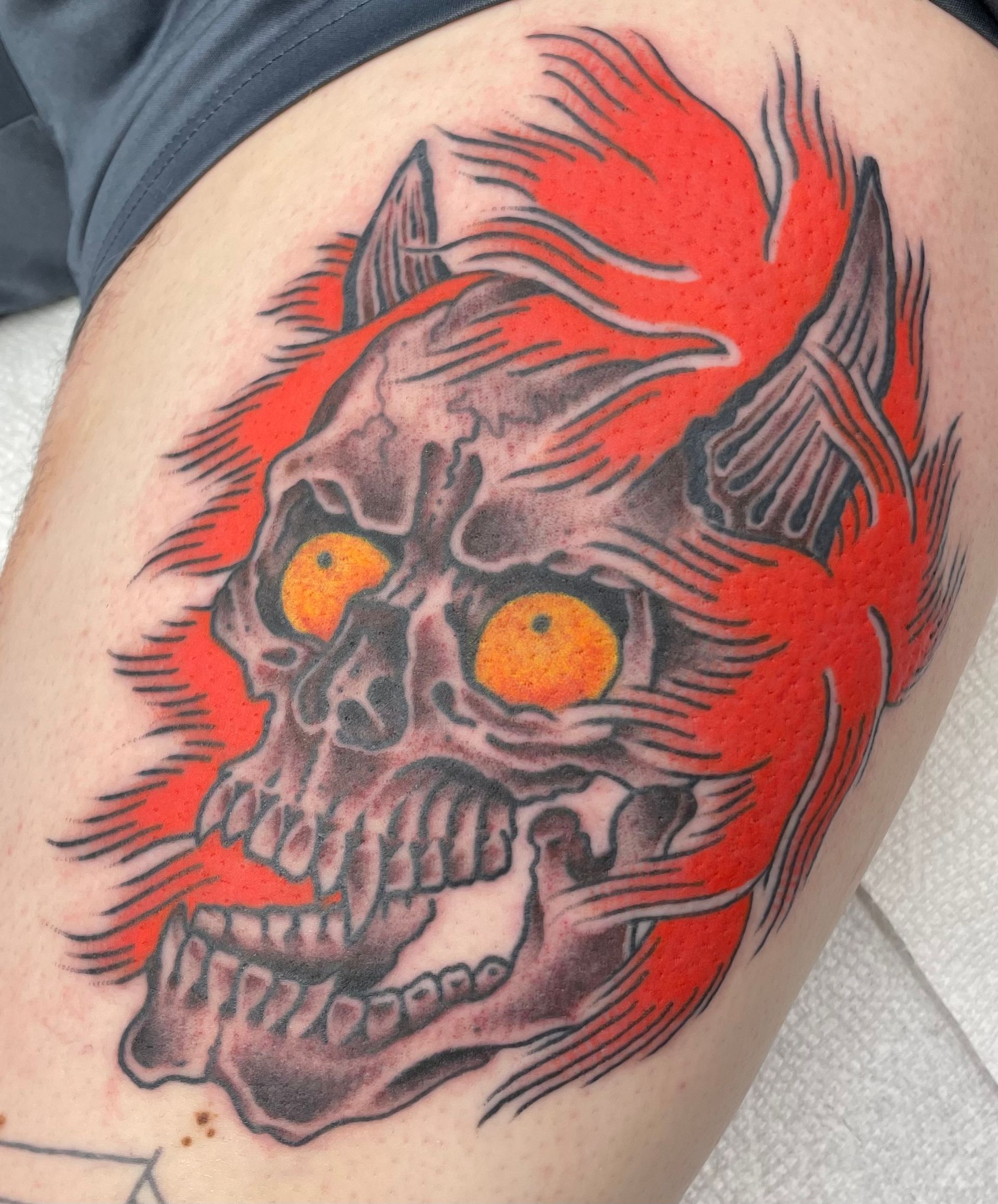 Red and black skull tattoo with flaming hair and glowing orange eyes on skin