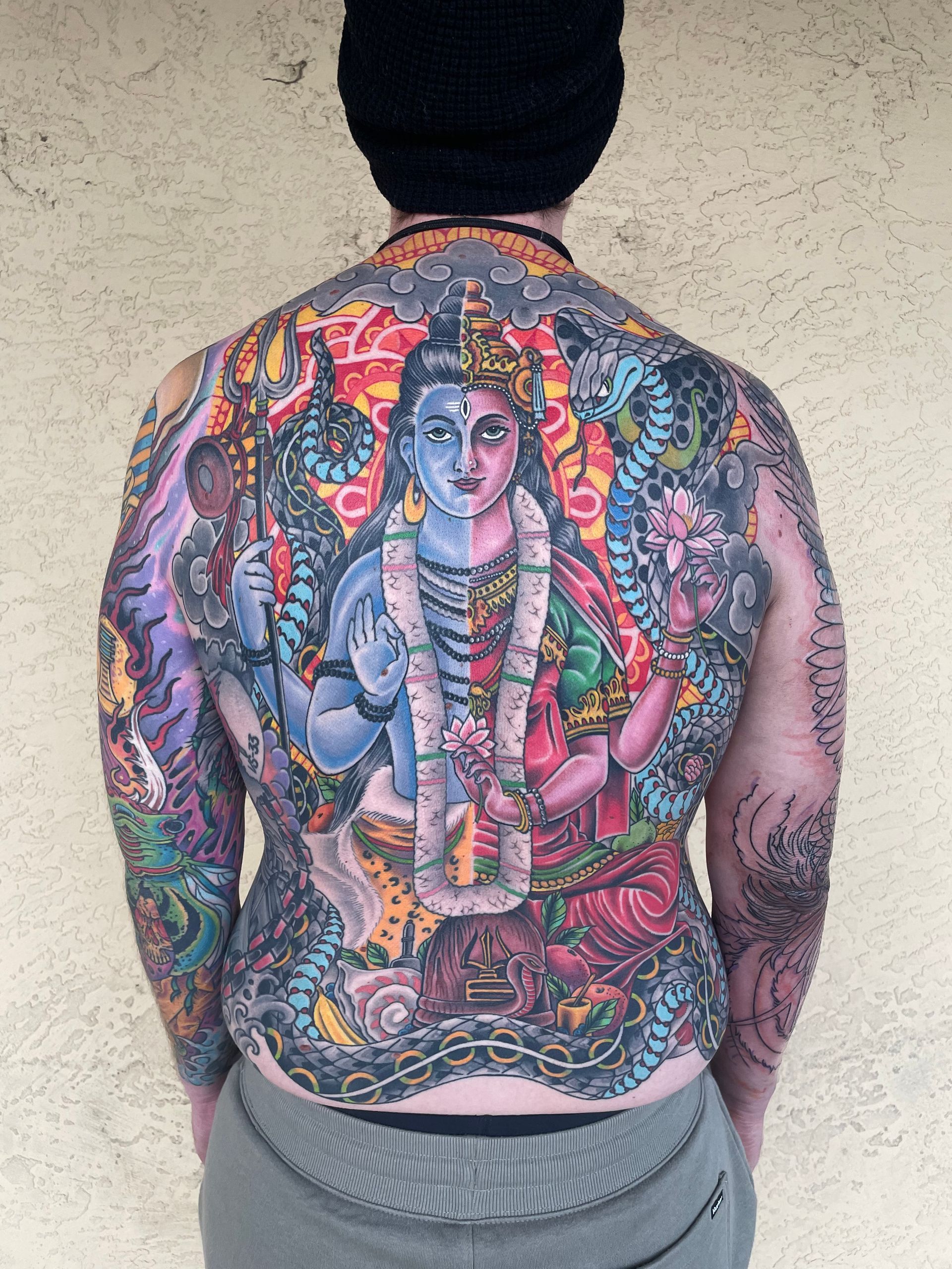 Back view of a colorful full-back tattoo featuring a Hindu deity, flowers, and ornate patterns.