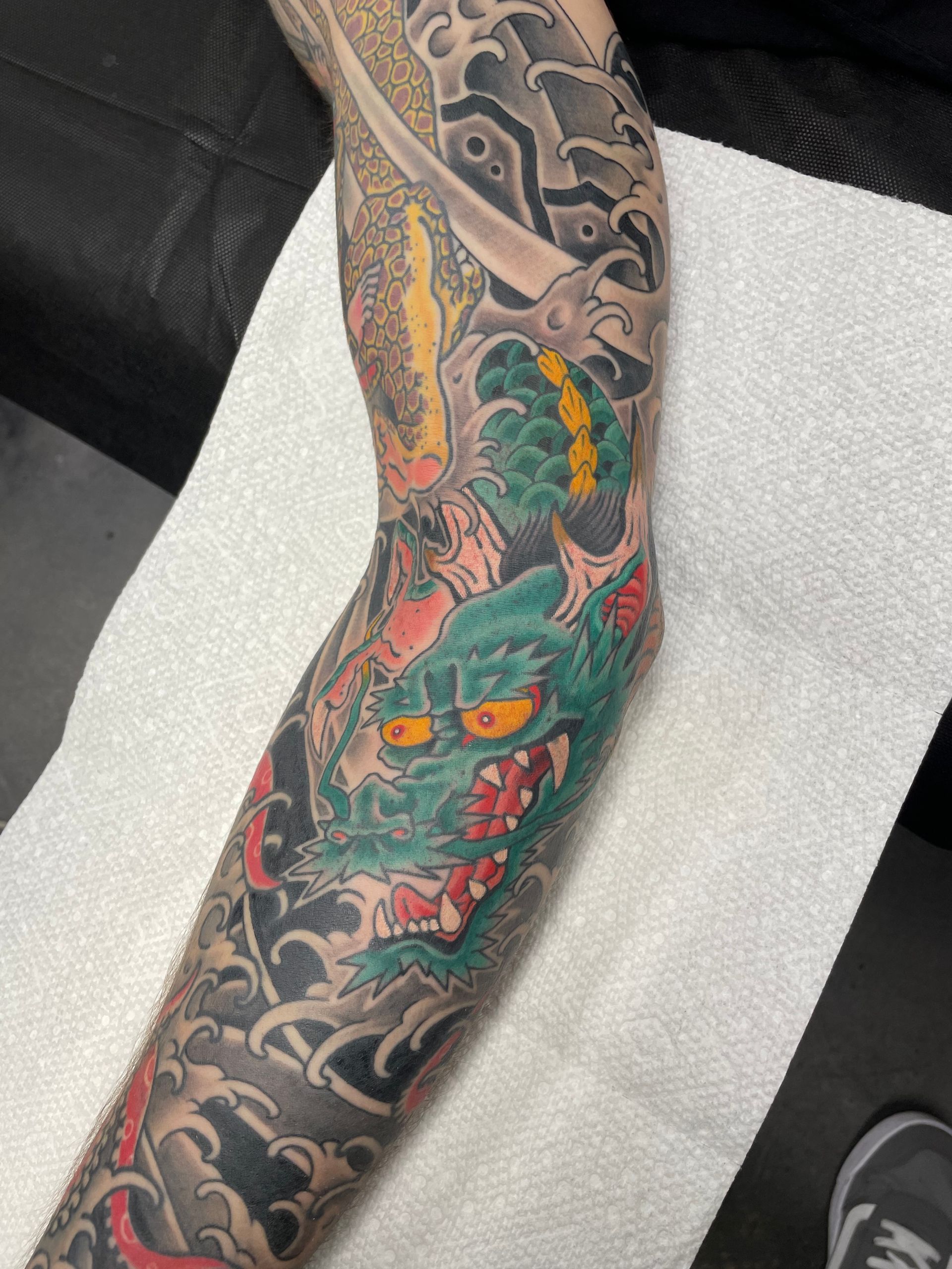 Close-up of a colorful dragon tattoo on a forearm with black and gray cloud patterns