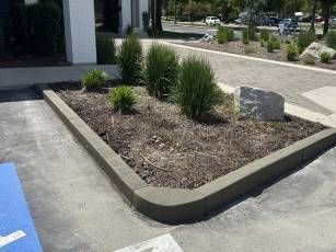 A concrete curb with a planter in the middle of a parking lot.