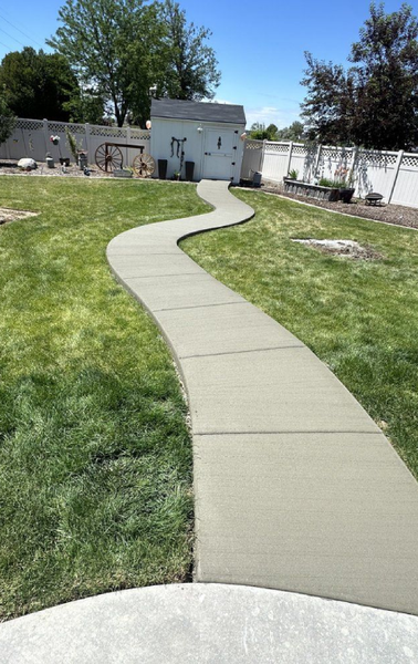 A concrete walkway going through a lush green yard.