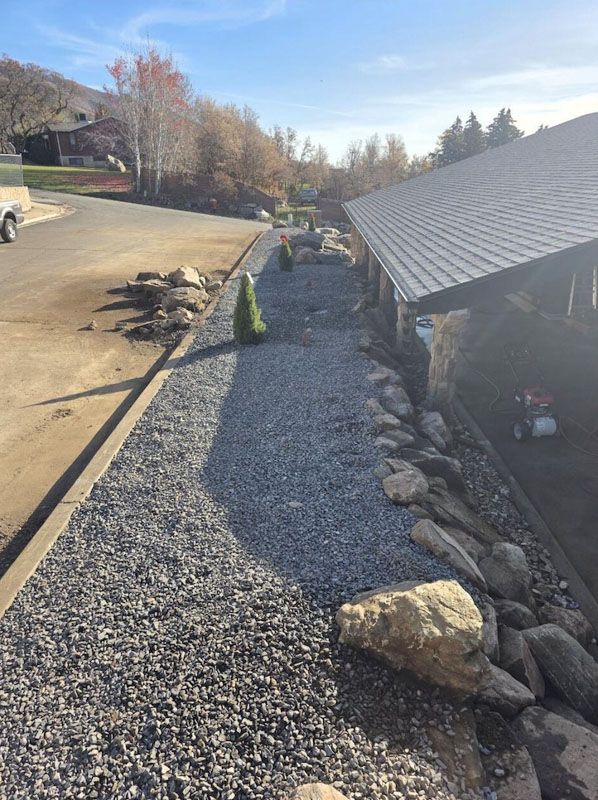 Gravel walkway beside a house with large rocks lining the edge on a sunny day