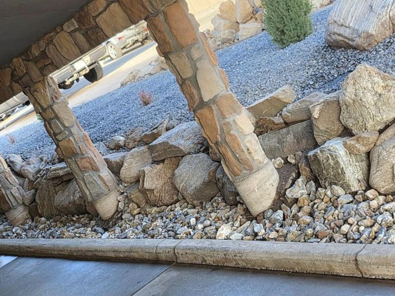 Stone retaining wall and support columns over blue gravel, with rocks and a curb in the foreground