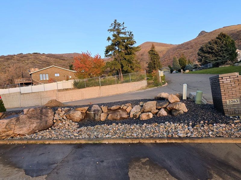 Rock and gravel landscape border beside a road with houses and hills in the background